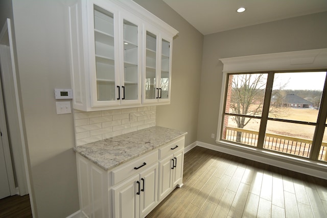 bar with light stone countertops, wood-type flooring, white cabinets, and tasteful backsplash