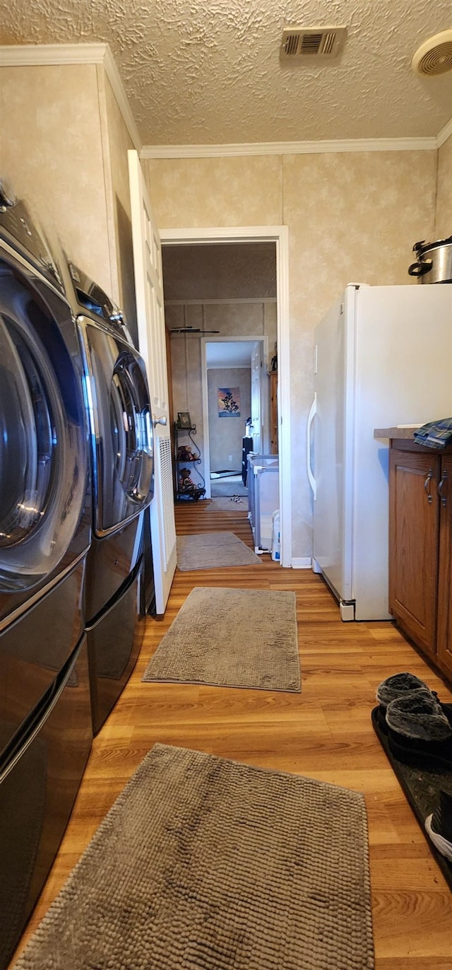 clothes washing area featuring a textured ceiling, ornamental molding, light hardwood / wood-style flooring, and washing machine and clothes dryer