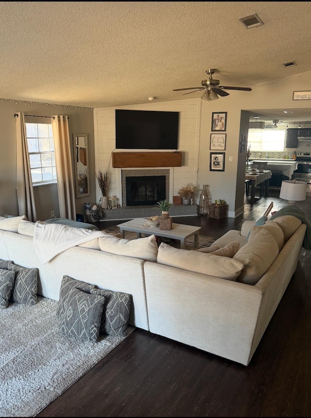 living room with ceiling fan, hardwood / wood-style floors, a fireplace, and a textured ceiling