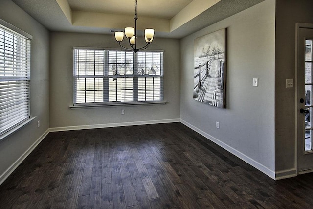 unfurnished dining area featuring dark wood-type flooring, an inviting chandelier, and a tray ceiling