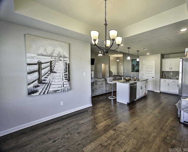 kitchen with pendant lighting, appliances with stainless steel finishes, white cabinetry, sink, and a center island with sink