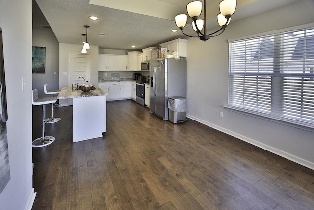 kitchen featuring a center island with sink, appliances with stainless steel finishes, white cabinetry, and decorative light fixtures