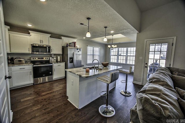 kitchen with stainless steel appliances, an island with sink, hanging light fixtures, light stone counters, and a breakfast bar area