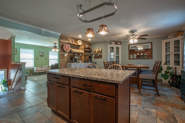 kitchen featuring a center island, crown molding, hanging light fixtures, ceiling fan, and light stone counters