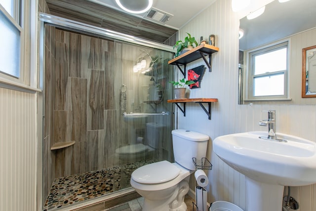 bathroom with a shower with shower door, sink, toilet, and wood walls