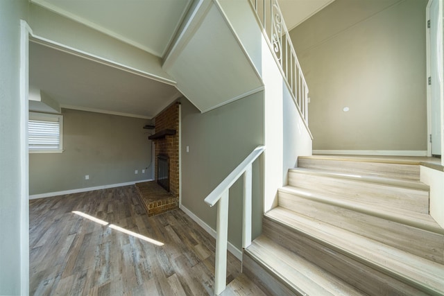 staircase with a brick fireplace, hardwood / wood-style flooring, and crown molding