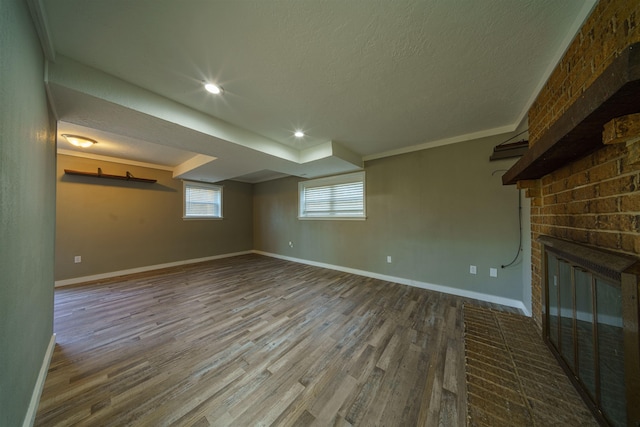 basement with wood-type flooring, a brick fireplace, crown molding, and a textured ceiling