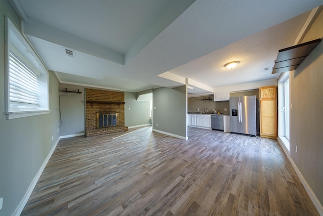 unfurnished living room featuring a healthy amount of sunlight, a brick fireplace, and hardwood / wood-style floors