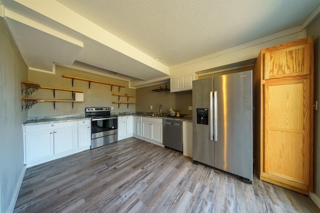 kitchen featuring light stone countertops, white cabinets, appliances with stainless steel finishes, light hardwood / wood-style floors, and sink