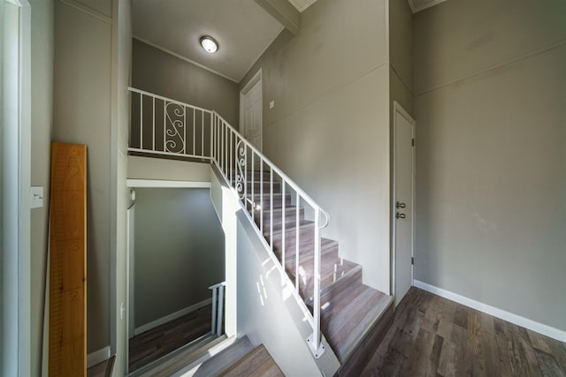 staircase with a high ceiling, beam ceiling, and hardwood / wood-style floors