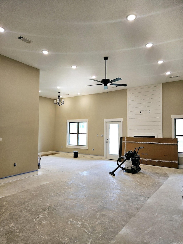 unfurnished room with ceiling fan with notable chandelier and a large fireplace