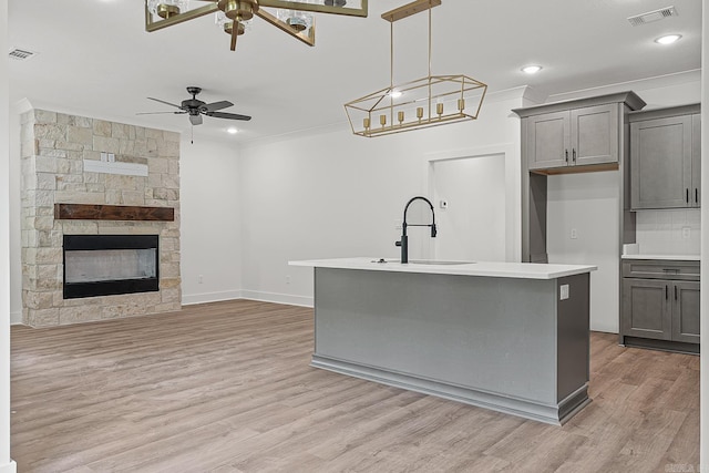 kitchen with pendant lighting, a fireplace, sink, ceiling fan, and a center island with sink