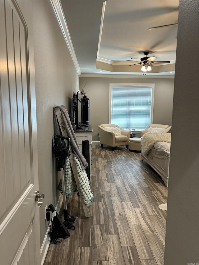 bedroom featuring ceiling fan, ornamental molding, wood-type flooring, and a raised ceiling