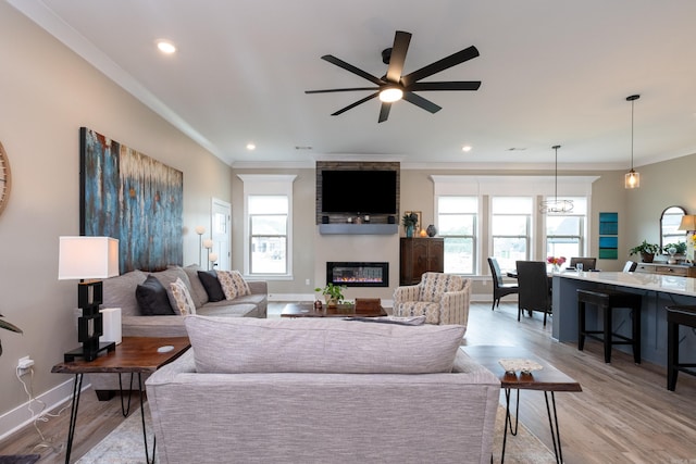 living room with ceiling fan, a large fireplace, ornamental molding, and light hardwood / wood-style floors