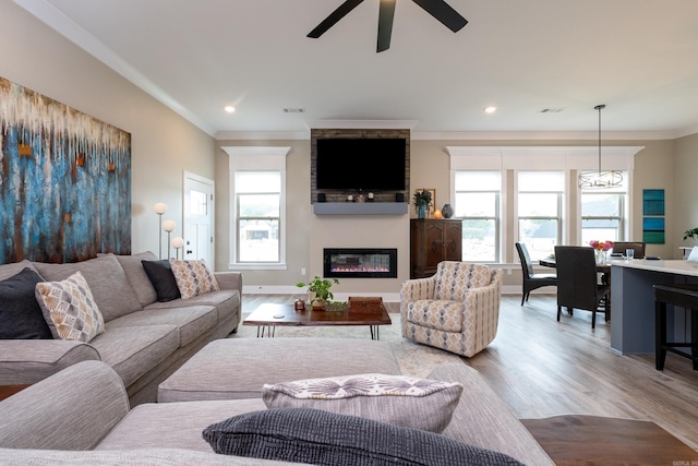 living room with ceiling fan, a large fireplace, ornamental molding, and light hardwood / wood-style flooring