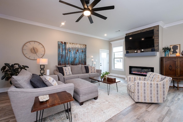 living room featuring ceiling fan, a large fireplace, light hardwood / wood-style flooring, and crown molding