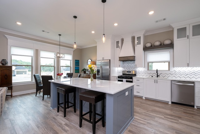 kitchen featuring decorative light fixtures, a kitchen island, custom exhaust hood, appliances with stainless steel finishes, and white cabinets