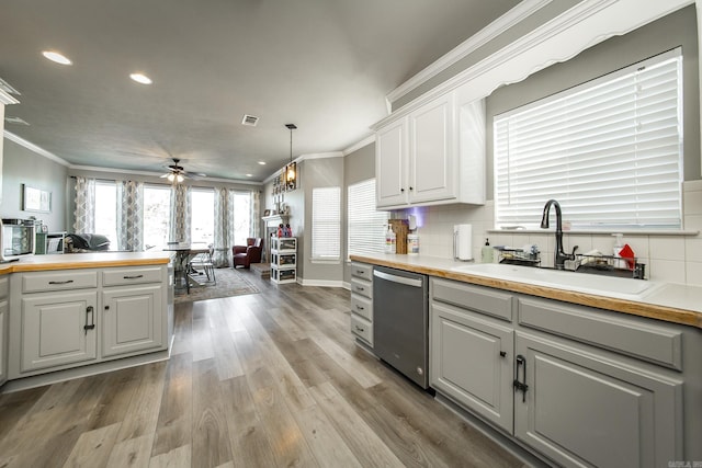 kitchen featuring white cabinetry, sink, hanging light fixtures, light wood-type flooring, and stainless steel dishwasher