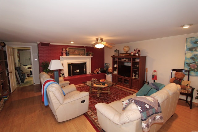 living room featuring ceiling fan, ornamental molding, a fireplace, and wood-type flooring