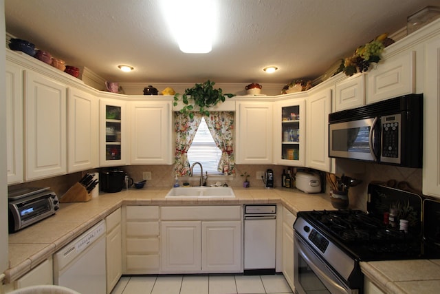 kitchen with light tile patterned floors, appliances with stainless steel finishes, tile counters, white cabinets, and sink