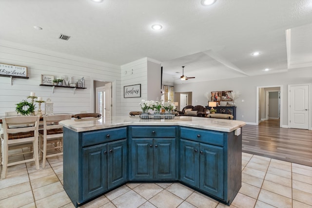 kitchen with light tile patterned flooring, blue cabinetry, wood walls, and a kitchen island