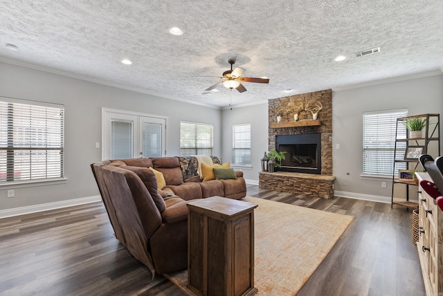 living room featuring dark wood-type flooring, a wealth of natural light, crown molding, and a stone fireplace