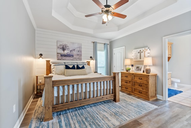 bedroom with ensuite bathroom, hardwood / wood-style flooring, ceiling fan, a tray ceiling, and ornamental molding