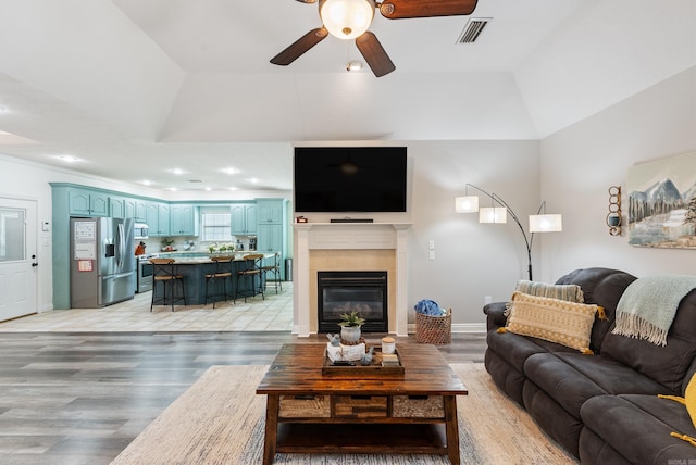 living room with hardwood / wood-style flooring, a tile fireplace, a raised ceiling, and ceiling fan