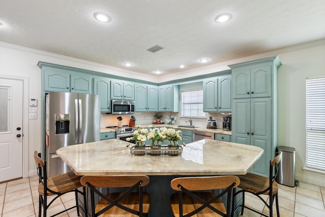 kitchen with light tile patterned floors, stainless steel appliances, ornamental molding, and a center island