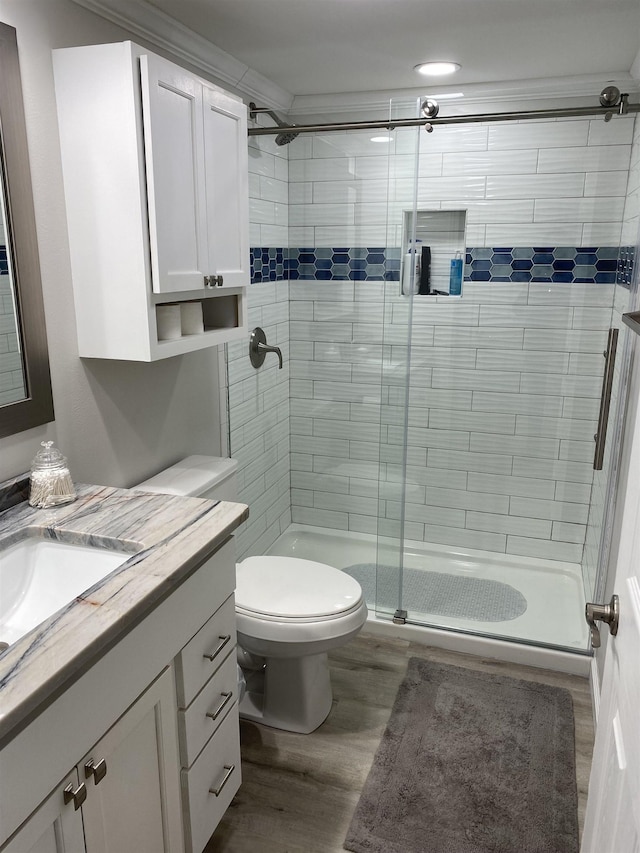 bathroom featuring toilet, vanity, hardwood / wood-style floors, crown molding, and a shower with shower door