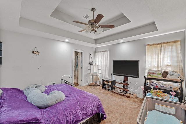 carpeted bedroom with ceiling fan, a tray ceiling, and a textured ceiling