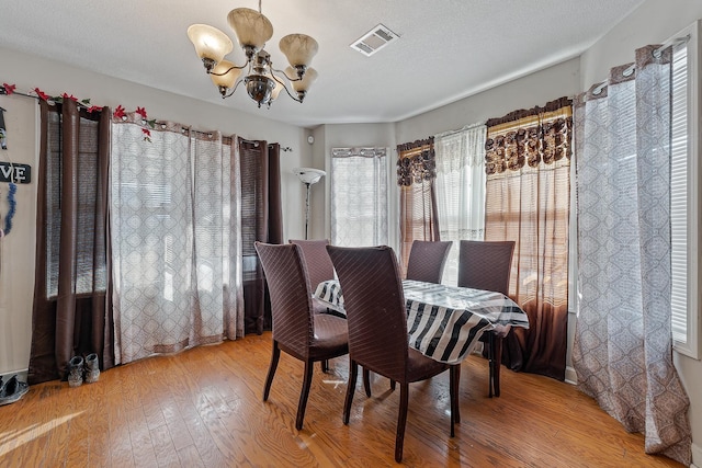 dining space with light hardwood / wood-style floors, a textured ceiling, and a notable chandelier