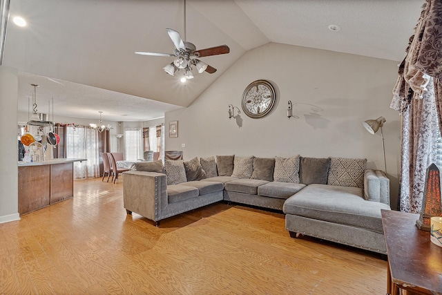 living room featuring ceiling fan with notable chandelier, light hardwood / wood-style flooring, and vaulted ceiling