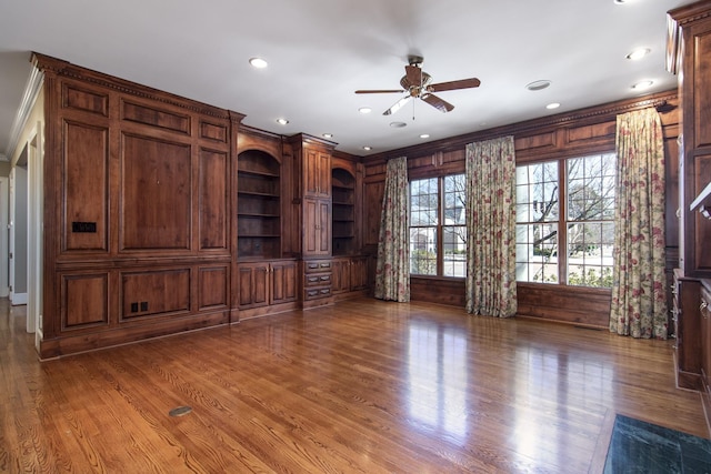 unfurnished living room featuring ceiling fan, crown molding, wood walls, and hardwood / wood-style floors