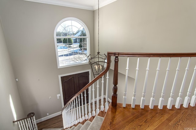 stairs featuring crown molding, wood-type flooring, and an inviting chandelier