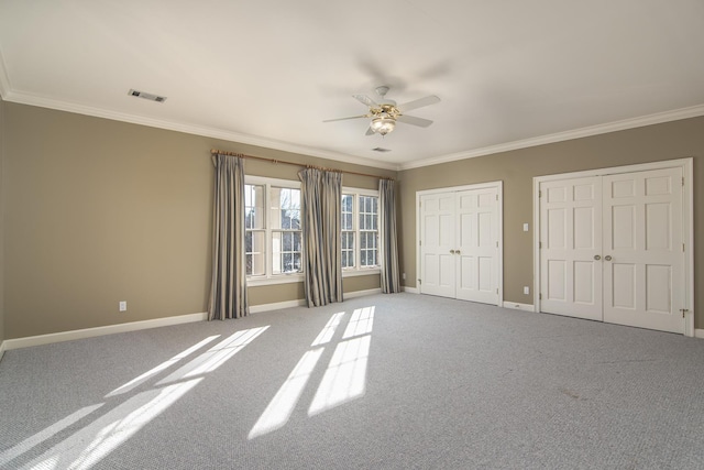 unfurnished bedroom with ceiling fan, two closets, carpet floors, and ornamental molding