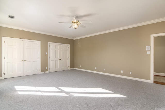 unfurnished bedroom featuring ceiling fan, two closets, carpet, and ornamental molding