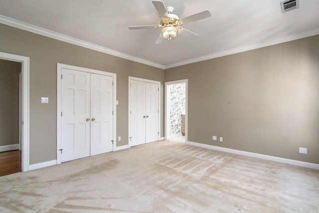 unfurnished bedroom featuring ceiling fan, two closets, crown molding, and light carpet