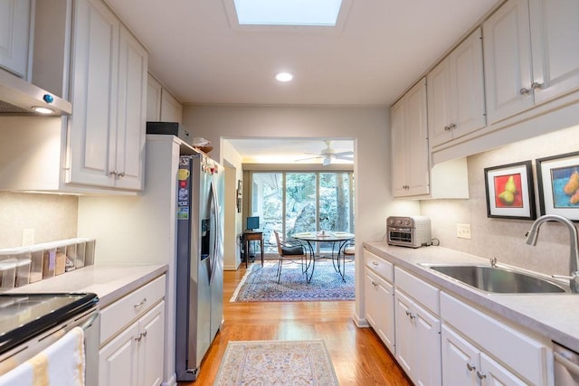 kitchen with sink, white cabinetry, a skylight, and light wood-type flooring