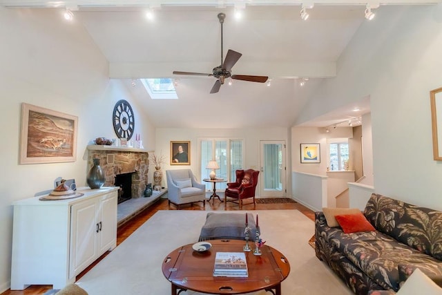 living room featuring ceiling fan, a fireplace, lofted ceiling with skylight, hardwood / wood-style flooring, and rail lighting