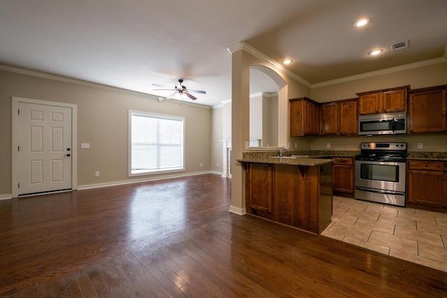 kitchen with kitchen peninsula, a kitchen bar, sink, appliances with stainless steel finishes, and ornamental molding