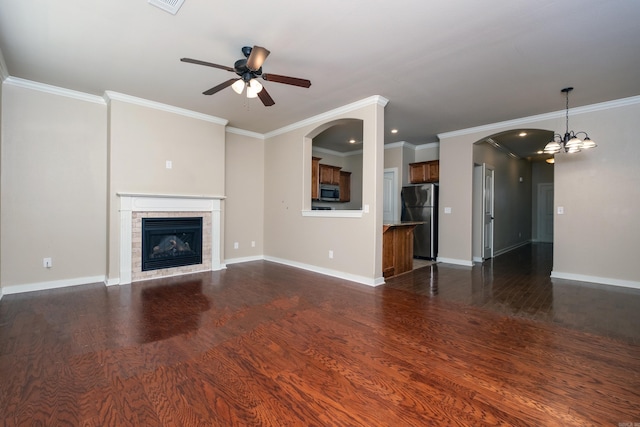 unfurnished living room with ceiling fan with notable chandelier, dark wood-type flooring, a tile fireplace, and crown molding