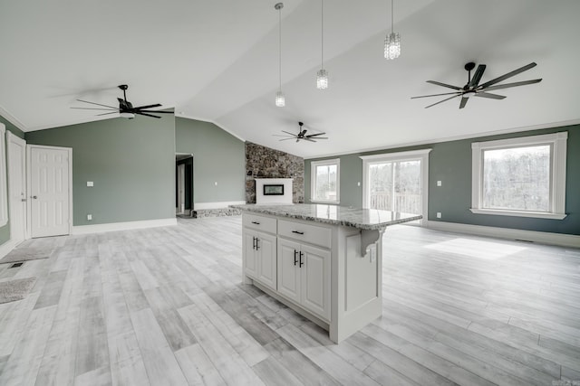 kitchen with lofted ceiling, hanging light fixtures, light stone countertops, a kitchen island, and white cabinets