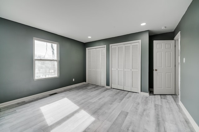 unfurnished bedroom featuring multiple closets and light hardwood / wood-style flooring