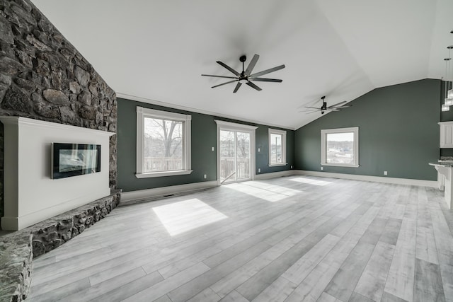 unfurnished living room with vaulted ceiling, ceiling fan, light hardwood / wood-style floors, and a stone fireplace