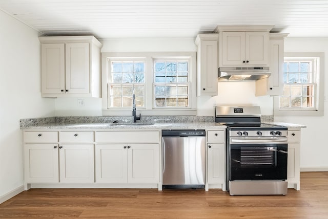 kitchen with light stone countertops, appliances with stainless steel finishes, white cabinetry, sink, and light wood-type flooring