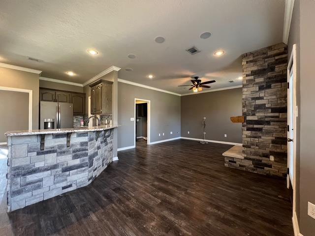 unfurnished living room with dark wood-type flooring, ornamental molding, sink, and ceiling fan