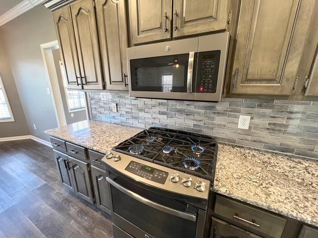 kitchen with tasteful backsplash, dark wood-type flooring, light stone countertops, appliances with stainless steel finishes, and ornamental molding