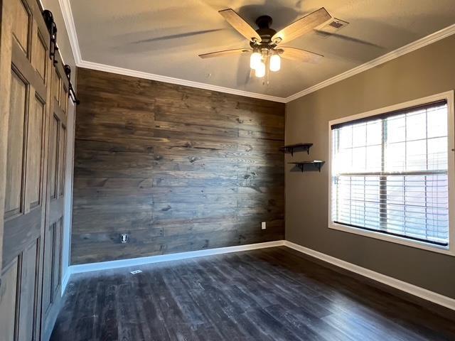 spare room with a barn door, wood walls, ceiling fan, dark hardwood / wood-style flooring, and crown molding