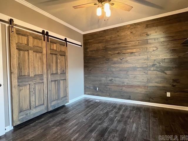 unfurnished bedroom with ceiling fan, a barn door, dark hardwood / wood-style flooring, and ornamental molding